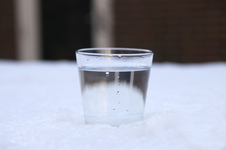 Glass filled with fresh clear cold water in the snowの写真素材