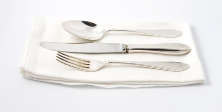 Silver spoon, knife and fork on white linen napkinの写真素材
