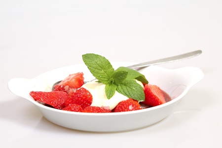 Bowl of strawberries with cream, strawberry liquor, a spoon and some and mint の写真素材