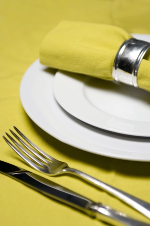 table setting with napkin, silverware and plates on yellow tableclothの写真素材