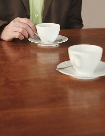Businessman drinking coffee at table with second cup in front of him. Focus on his hand and cupの写真素材