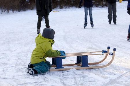 THE NETHERLANDS-FEB 4:Small boy sitting on ice with sleigh looking at skaters on feb 4, 2012. February is the coldest month throughout the Netherlands with an average of -0.5¡C. This february although temperatures dropped to a minus 20 ¡Cのeditorial素材