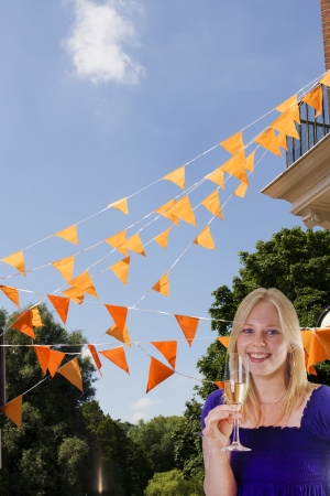 Blonde woman with champagne in front of orange flagsの写真素材