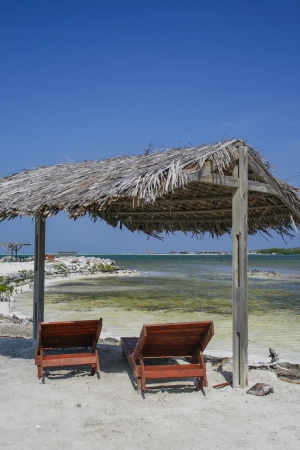 two wooden reclining chairs under a thatched roof on the beach in Bonaireの写真素材