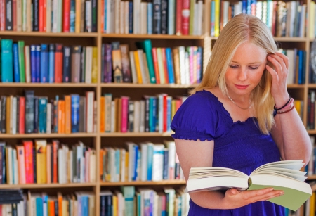 Blonde girl reading book in front of full bookshelves の写真素材
