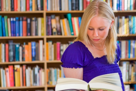 Blonde girl reading a book in front of bookcaseの写真素材
