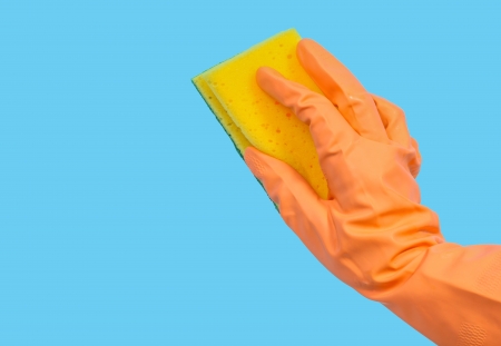 Orange gloved hand cleaning with sponge on blue backgroundの写真素材