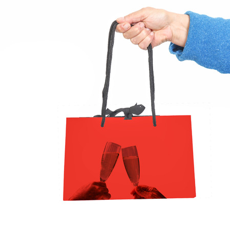 Hand in blue sweater holding red bag with image of two champagne glasses toastingの写真素材