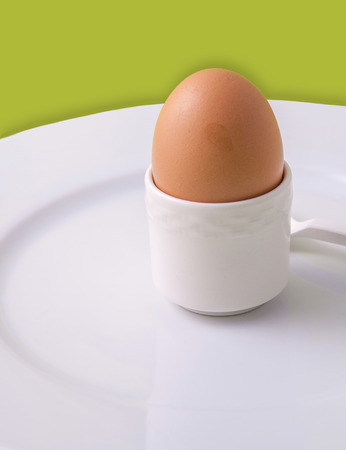 An egg in an eggholder on a white plateの写真素材