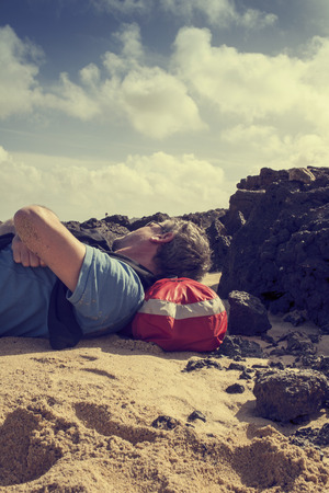 Man lying down on the beach in Lanzarote, Spain resting his head on his backpackの写真素材