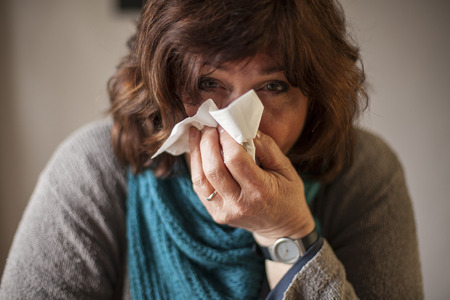 Ill woman with blue scarf and handkerchieif blowing noseの写真素材