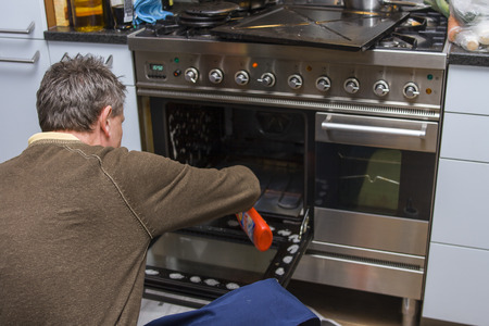 A man kneeling on the kitchen floor and cleaning the inside of an oven.

の写真素材