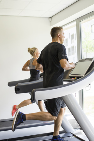 Healthy man and woman running on a treadmill in a gymの写真素材
