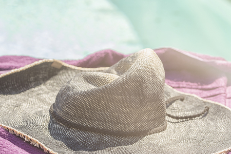 Summer concept. Straw sun hat on a purple towel with a blue water backgroundの写真素材