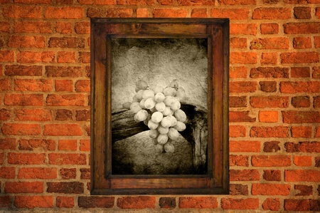 Grapes in an old wooden frame hanging on a brick wallの写真素材