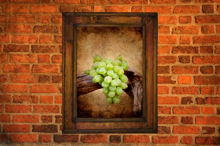 Green grapes in an old wooden frame hanging on a brick wallの写真素材