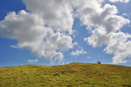 A green hill under a deep blue sky and white cloudsの写真素材