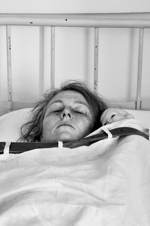 Woman with doll tied up in bed in a psychiatric ward.の写真素材