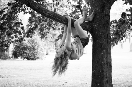 Yong girl with long blond hair hanging from tree in park. Black and white.