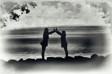 Artistic, crackled, black and white image of silhouettes of two ypung women making a formation with their arms.の写真素材