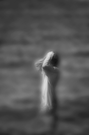 Surreal blurred black and white image of unrecognizable woman standing in water.の写真素材