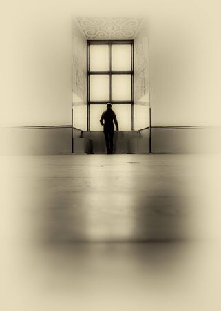 Artistic textured image of unrecognizable woman silhouette standing in front of large windowの写真素材