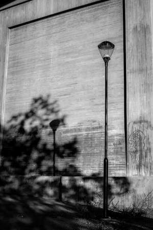 Old lamp post against concrete wall with heavy shadows.の写真素材