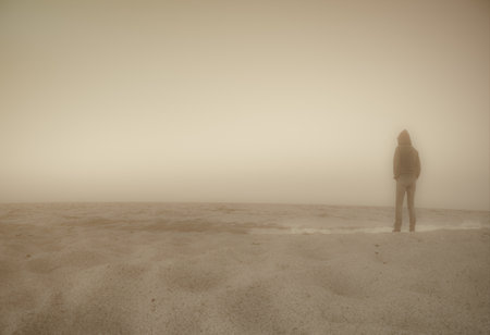 Dreamlike monochrome image of lonely person standing on empty beach looking out over the water.の写真素材