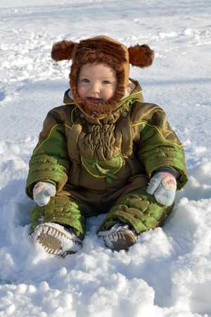 Little boy sitting in the snow in winter park and smiling.の写真素材