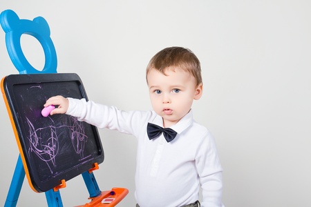 Little boy draws with chalk something on blackboard