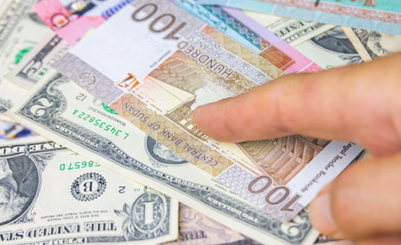 Male hand hold100 Sudanese pounds banknote with US dollars, the currency of Sudan. Close up Paper Money of the arabic country with high inflation. Old man hands shows money. Hand with money,の写真素材