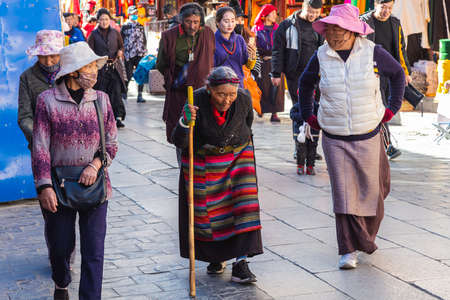 Lhasa, Tibet, China - November 15, 2020:  Old Tibetan woman in traditional Tibetan clothes and walking stick. For prayer purpose people walking on the  bakuo road around the Jokhang Temple.のeditorial素材