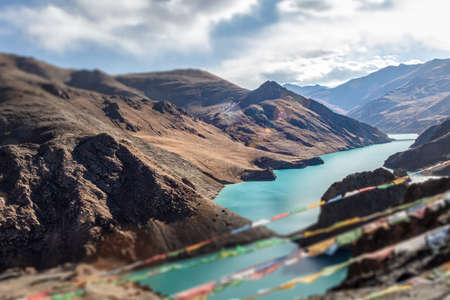 Kong mu Co Lake at 5000 meter above sea level at Tibet. Colorful prayer flags in front waving in the wind. Turquoise water in the mountain lake. Tilt shift effect brings strong visual effectの写真素材