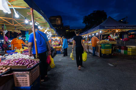 Street food night market at  Putrajaya, near Kuala Lumpur. Young woman walks between the food stands and carries her purchases in yellow plastic bagsのeditorial素材