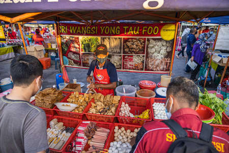 A tofu seller at the street fresh market Putrajaya, Kuala Lumpur. Customers wait for the seller to pack their goods. Man with face mask sells tofuのeditorial素材