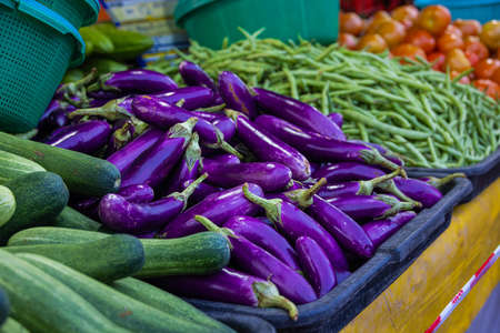 Vegetables on a counter of a vegetable shop in the fresh market. Aubergine or eggplant, beans and cucumber on the counter of the stand. The Putrajaya, Malaysia fresh market at Friday night.の写真素材