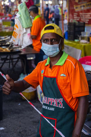 Kuala Lumpur, Malaysia - October 16, 2020: Seller at a chicken rice shop on a street market shows thumbs up in the corona crisis. Man with face mask shows optimism in the crisis. Live goes onのeditorial素材