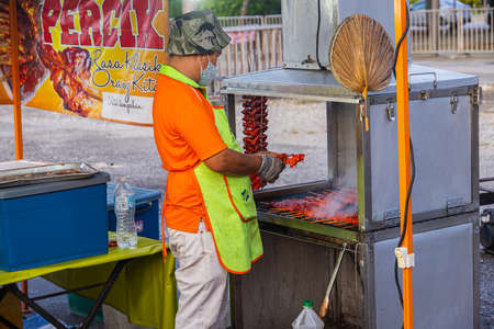 Honey chicken shop on the night market at Putrajaya, Kuala Lumpur. Man grills the marinated chicken on a small grill. The meat has a strong red colorのeditorial素材