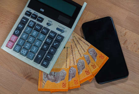 20 malaysian Ringgit on a wooden desk, surrounded of calculator and a mobile phone.  Close up macro...