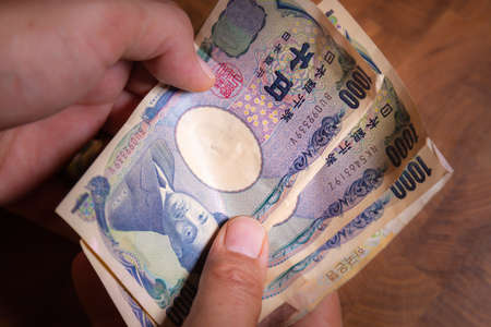 Male hands shows Japanese yen. Yen is the currency of Japan. On the Obverse side of the banknotes Hideyo Noguchi, bacteriologist from the 20th century. Paper Money from Japan. Banknote with low valueの写真素材