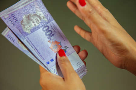 Female Hands with red nails counting 100 Ringgit banknotes. Ringgit the currency of Malaysia. Woman hands showing RM100 notes. Close up to the Malaysian money with colorful fingernailsの写真素材