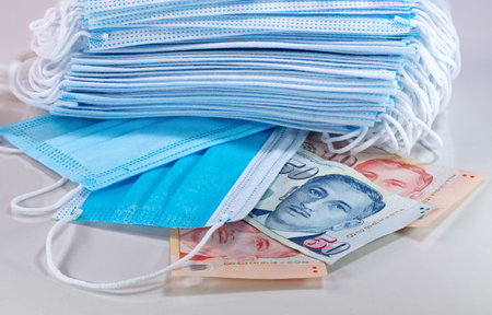 Face masks, the new world currency in 2020. Corona Cov19 crisis makes face mask to the most wanted equipment. Prices rising up. Mouth mask with Singapore dollar money on a white background.の写真素材