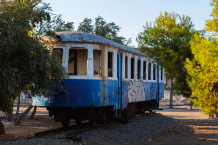 Lavrio, Greece - July 28, 2021: Old tram in a park in Lavrio. Covered in graffiti and without window glass. Discarded tram between trees in a park. Museum piece of former public transportのeditorial素材