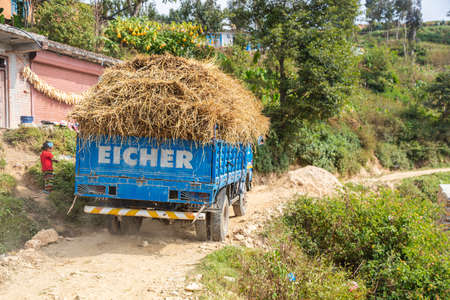 Kathmandu, Nepal - October 29, 2021: Truck overloaded with hay, on a dirt mountain road. Blue lorry on unpaved road in the mountains. On one side of a steep mountain slope. Moving slowly to avoid accidentsのeditorial素材