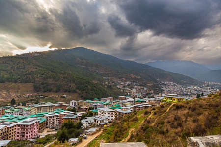 Thimphu, Bhutan - October 26, 2021: Aerial view cityscape of Bhutan capitol city. Top view with dramatic cloudy sky over the town. Largest city in Bhutan in a mountain valley. Houses with green roofsのeditorial素材