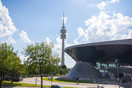 Munich, Germany - July 6, 2022: View past the glass facade of BMW World to the Munich Olympia Park with the Olympia Tower (Olympiaturm). Tower serves as a broadcast tower and has an observation deckのeditorial素材