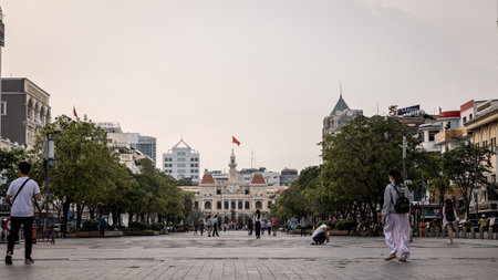 Ho Chi Minh City, Vietnam - November 07, 2022: City Hall on the national square in Saigon. Cityscape of the Indochina metropolis. People walking on the sidewalk. Vietnamese flag on the clock towerのeditorial素材