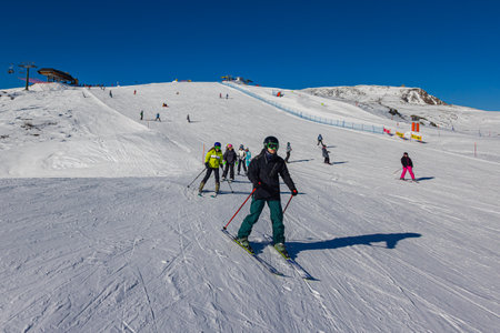 Falcade, Italy - February 15, 2023: Ski slope with skier under blue sky. People drive down the snowy mountains on skis. Group of skiers on a ski slope in the winter season. Winter sports activitiesのeditorial素材
