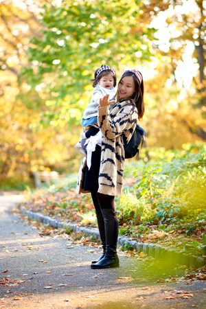Mother holding daughter in stunning fall scene in the parkの写真素材