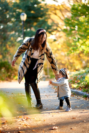 Mother holding daughter in stunning fall scene in the parkの写真素材
